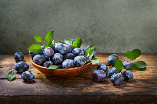 blue plums with leaves in a bowl on wooden table