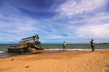Fototapeta na wymiar Wreck of the boat ruins the beach and slihouette of fisherman while fishing.