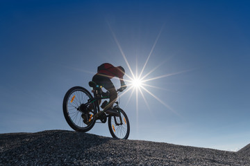 Young man riding mountain bike on the background of mountains at blue sky