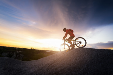 Young man riding mountain bike on the background of mountains at sunset