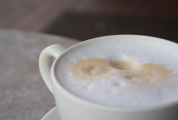 Tasse Kaffee mit aufgeschäumter Milch auf einem Bistrotisch im Freien