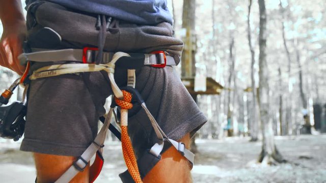 Putting on climbing equipment close-up 4K. Long shot close-up of person lower torso in focus while attaching the climbing safety equipment. The background forest desaturated.