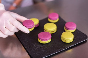 Holding macaroons. Professional confectioner wearing white gloves holding nice pink and yellow macaroons