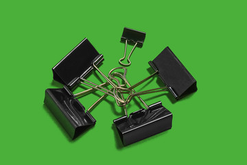 pile of black paper clips for office stationery lying on the green background. concept of business or educational equipment