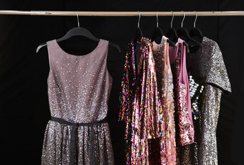 Row of sequins colorful sundress hanging on hanger– black background, 