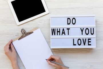 Work space with tablet, female hands, clipboard and 'Do what you love' word on modern board over white wooden background, top view. From above, flat-lay, overhead.