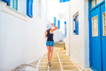 Young girl in white hat walking on a typical Mykonos street, back view