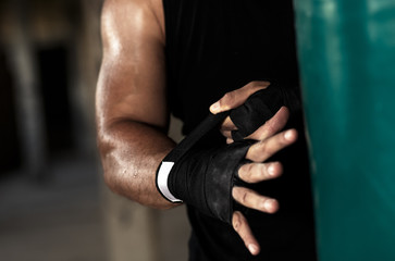 Male boxer bandage his hands before punching a boxing bag in warehouse.