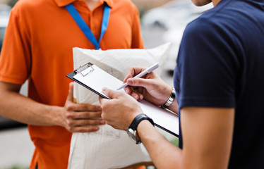 A person wearing an orange T-shirt and a name tag is delivering a parcel to a client, who is...