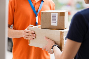A person wearing an orange T-shirt and a name tag is delivering parcels to a client. Friendly...