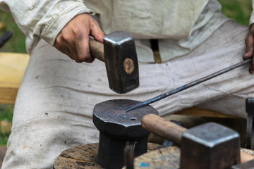 Blacksmithing, blacksmith in white cloth hits anvil with a hammer
