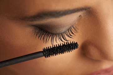 closeup of a young dark-skinned woman applying mascara on a white background - Powered by Adobe