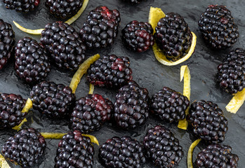Delicious fresh and ripe blackberries and reddish garnet. With drops of water. On textured background in black color.With yellow lemon rinds.