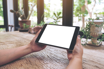 Mockup image of woman's hands holding black tablet pc with blank white screen on vintage wooden table