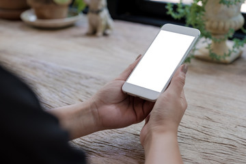 Mockup image of woman's hands holding mobile phone with blank white screen on wooden table in vintage cafe