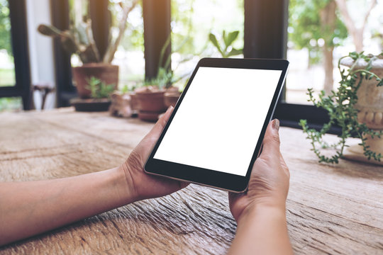 Mockup image of woman's hands holding black tablet pc with blank white screen on vintage wooden table