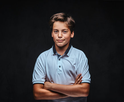 Portrait Of A Teenager Dressed In A White T-shirt Standing With Crossed Arms. Isolated On The Dark Background.