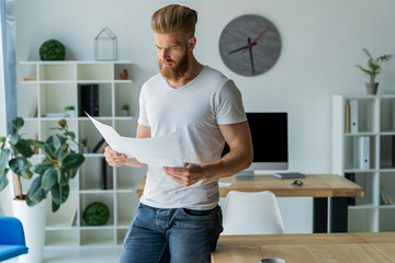Bearded young businessman working at modern office.Man wearing white t-shirt and making notes on the documents.