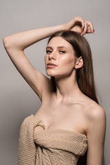 Portrait of a girl with natural make-up and bare shoulder. White background. Knitted sweater from the shoulder. Hand in hair. Long smooth hair.