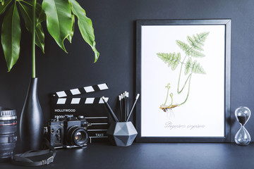 Minimalistic black desk with mock up photo frame, tropical leaf, photo camera, black accessories...