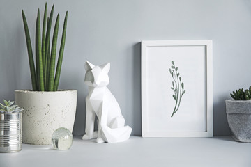 Gray modern space with mock up poster frame, fox figures and plant. Minimalistic desk in gray interior. 