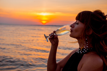 woman at sunset. Elegant girl is drinking champagne on romantic date in the evening. 
