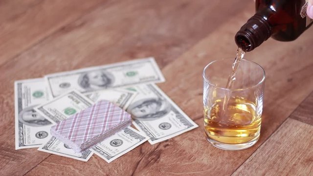 Pouring whisky into glass beside playing cards and dollar banknotes