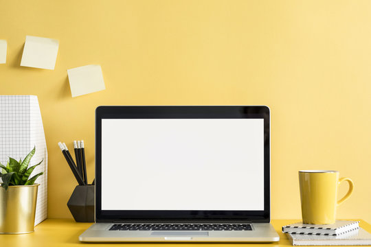 Stylish office workspace with laptop mock up screen, office accessories, plant, cup of coffee and memo sticks on the yellow wall. Design space for freelancer.