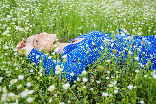 Portrait of a beautiful young woman lies among white wildflowers in a meadow and looks up