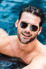 handsome smiling man in sunglasses looking at camera near poolside
