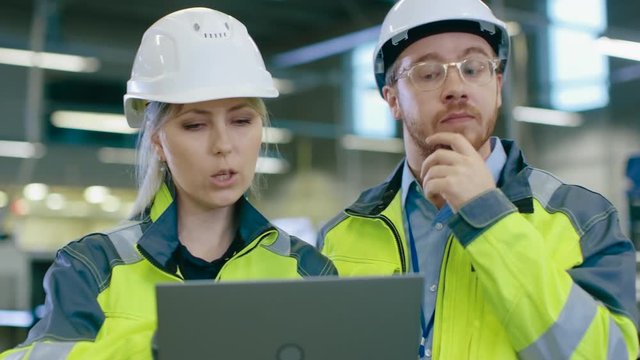 Male and Female Industrial Engineers Work on a Manufacturing Plant, They Discuss Project, Point in the Direction of the Machinery while Using Laptop. 
