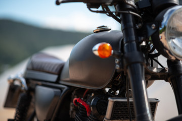 Side of the motorcycle classic black. There are many parts blurred by the sky and mountains.