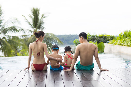 Happy young family sitting side by side at the pool
