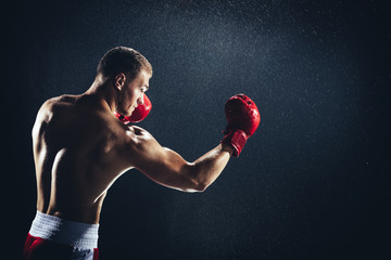 Man boxing with red gloves on his hands in the rain.