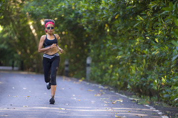 lifestyle outdoors portrait of young attractive and fit woman with hairband training hard on asphalt road running workout at beautiful trees city park