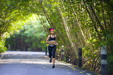 lifestyle outdoors portrait of young fit and happy Asian Korean woman with hairband training hard on asphalt road running workout at beautiful trees city park