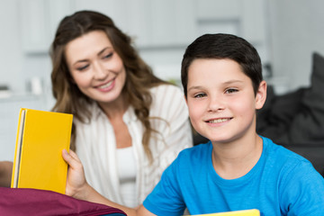 Obraz premium selective focus of smiling boy with book and mother behind at home