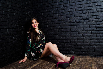 Portrait of a fabulous young woman in floral dress sitting in the dark studio.