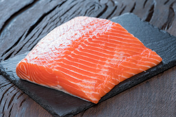 Fresh salmon fillet on black cutting board.