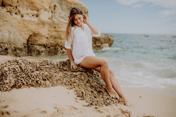 Fototapeta na wymiar Portrait of attractive blonde girl wears white shirt with long hair posing on deserted beach.