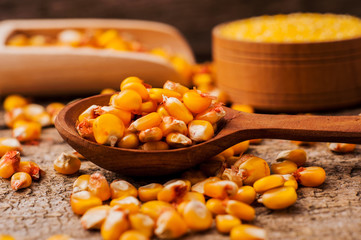 a bowl of corn is on a wooden table.Wooden spoon of grains of corn.Grains of corn