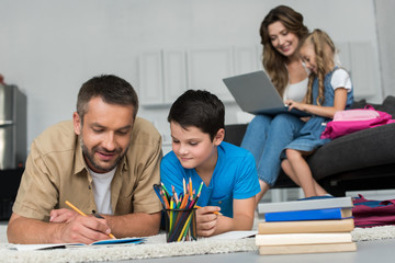 Fototapeta premium selective focus of father and son doing homework together while mother and daughter using laptop on sofa at home
