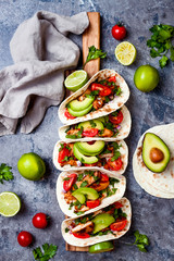 Mexican grilled chicken tacos with avocado, tomato, onion on rustic stone table. Recipe for Cinco de Mayo party. Top view, overhead, flat lay.