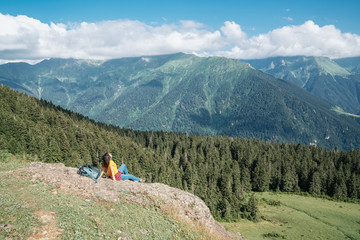 Young happy woman with backpack standing on a rock looking to a valley below