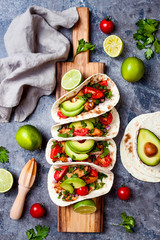 Mexican grilled chicken tacos with avocado, tomato, onion on rustic stone table. Recipe for Cinco de Mayo party. Top view, overhead, flat lay.