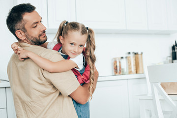 father and little daughter with backpack hugging each other in kitchen at home, back to school concept