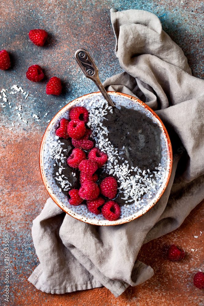 Wall mural Activated charcoal smoothie and chia seed pudding bowl, vegan detox dessert with raspberry and coconut milk. Overhead, top view, flat lay