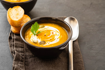 Pumpkin soup in a bowl with fresh pumpkins, garlic and parsley herbs on a black background. Autumn concept.