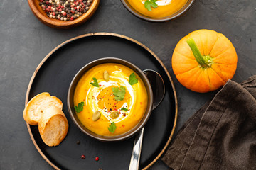 Pumpkin soup in a bowl with fresh pumpkins, garlic and parsley herbs on a black background. Autumn concept.