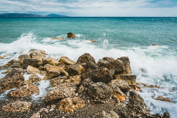 Fototapeta na wymiar Waves beat against stones on a sunny day in Crete, Greece. Blue Sea Ocean in the background and stone beach in the foreground.